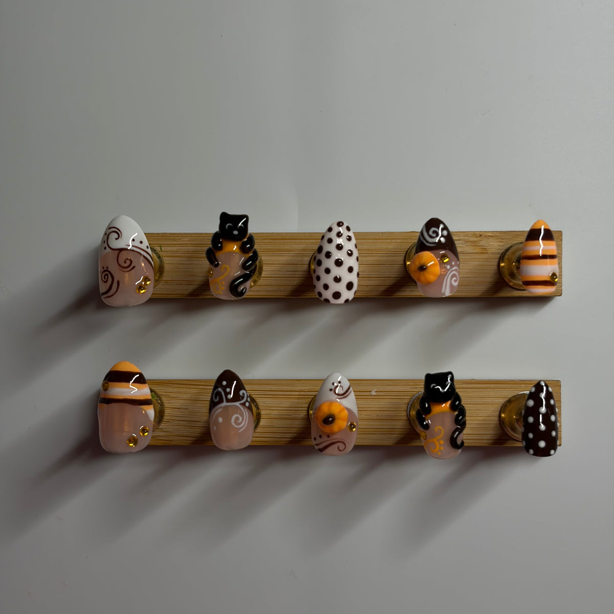 Two wooden peg racks mounted on a light gray wall, holding a row of hand-painted ceramic owl figurines in black, orange, white, and brown.